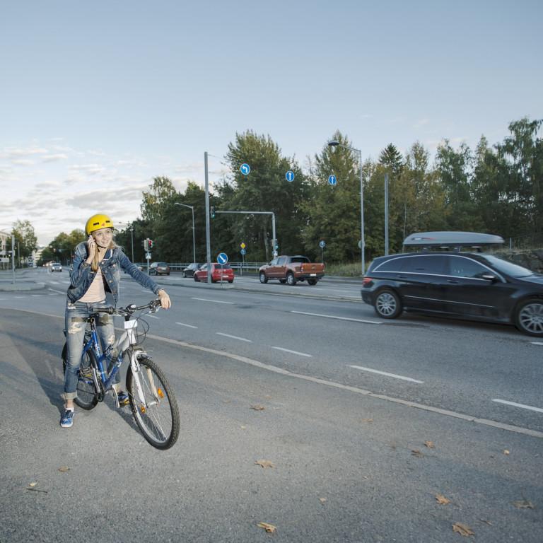 Kuvassa nuori pyöräilijä, joka on pysähtynyt ja puhuu kännykkään.