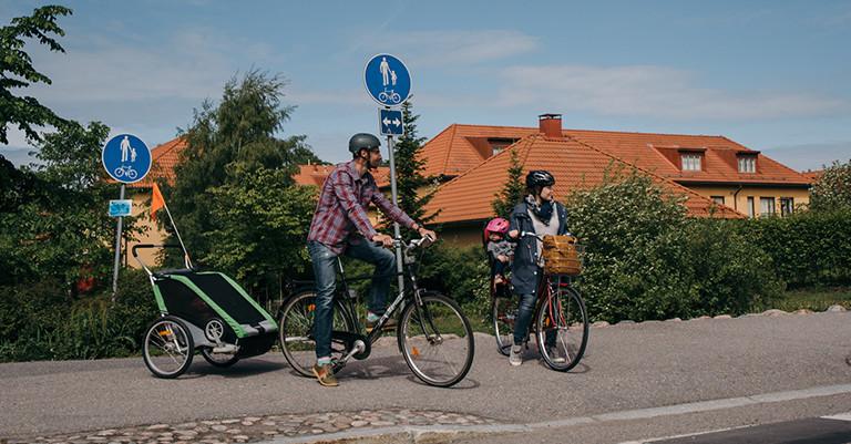 Kuvassa vanhemmat kyyditsevät lapsiaan polkupyörillä.