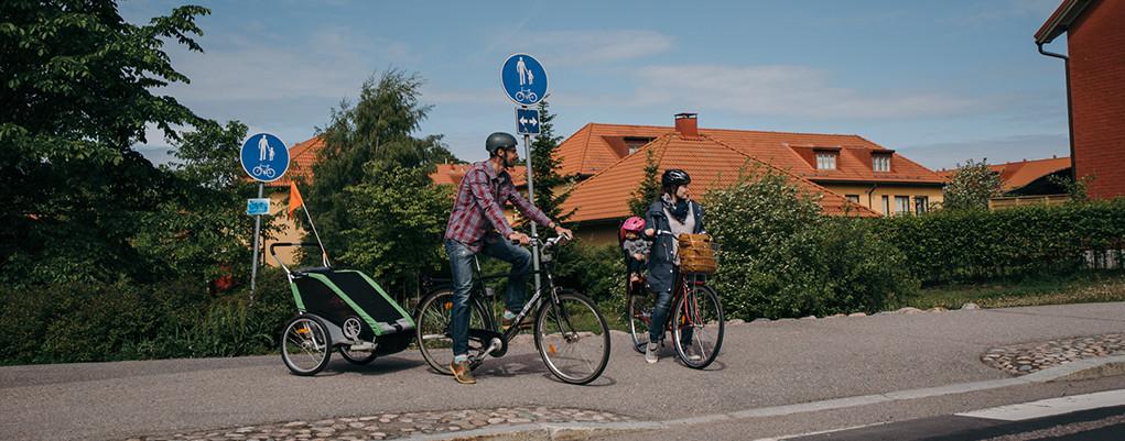 Kuvassa vanhemmat kyyditsevät lapsiaan polkupyörillä.