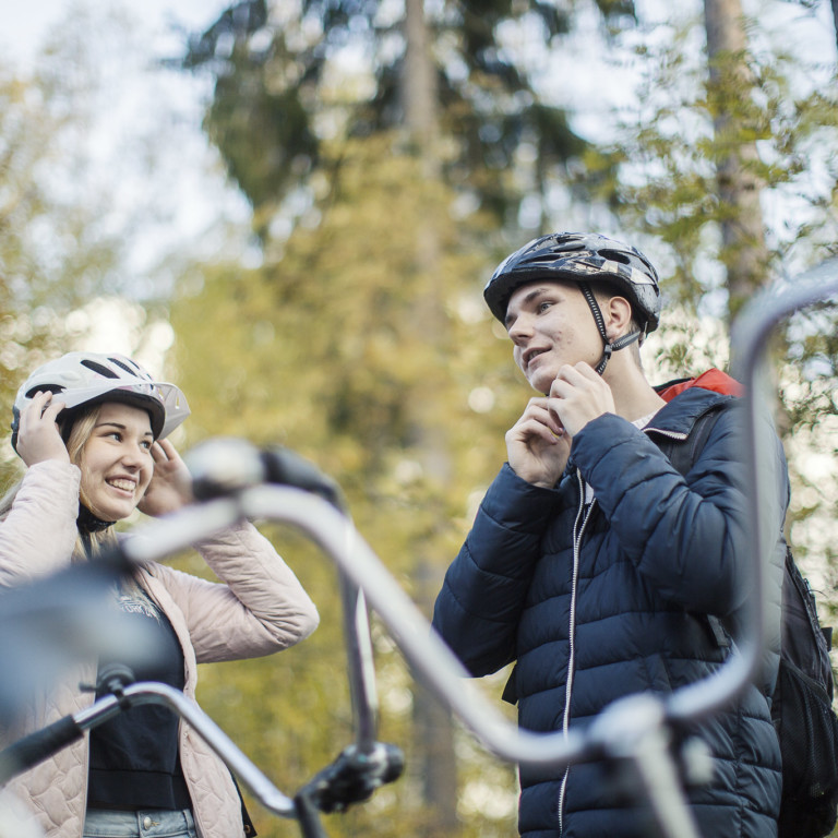 Kaksi nuorta pyöräilijää laittaa kypäriä päähän.