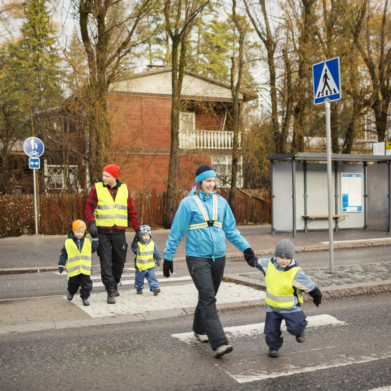 Lapset ja kaksi aikuista ylittää tien suojatietä pitkin.