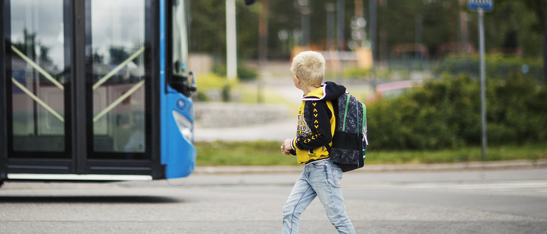 Pieni koululainen ylittämässä suojatietä. Taustalla bussi.