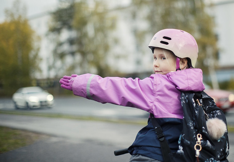 Pyöräilevä lapsi näyttää suuntamerkkiä kädellään.